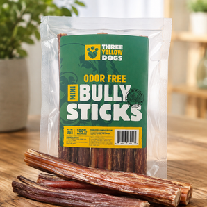 Bag of Three Yellow Dogs Odor Free Mini Bully Sticks standing on a wood table with a few loose bully sticks in front.